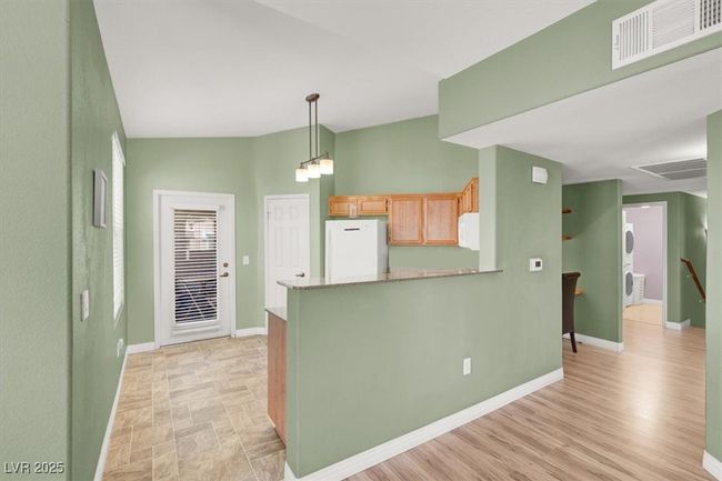 Kitchen with freestanding refrigerator, baseboards, visible vents, stacked washer and clothes dryer, and a peninsula | Image 13