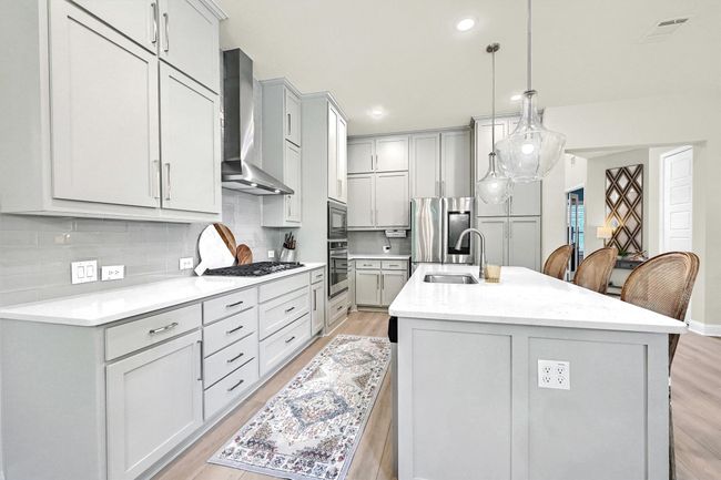 Kitchen featuring wall chimney range hood, an island with sink, light wood finished floors, backsplash, and appliances with stainless steel finishes | Image 12