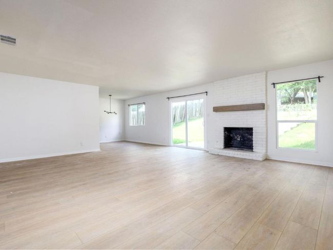 Unfurnished living room with light wood-style flooring, a brick fireplace, baseboards, and a chandelier | Image 6