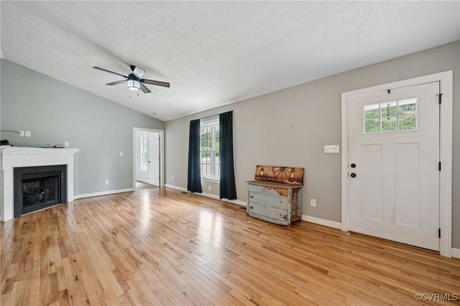 Unfurnished living room featuring light wood-style floors, a ceiling fan, vaulted ceiling, healthy amount of natural light, and a textured ceiling | Image 4