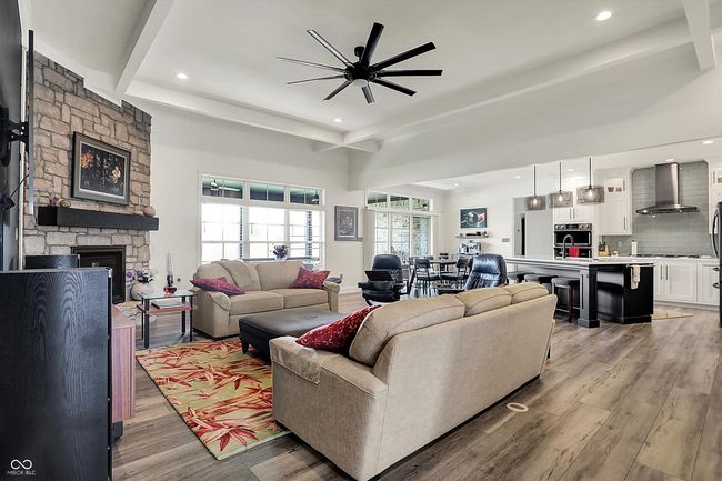 living area with beamed ceiling, a stone fireplace, light wood-type flooring, and ceiling fan | Image 8