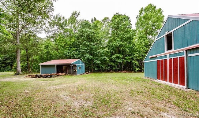 View of green lawn featuring a pole building, an outdoor structure, a garage, and view of wooded area | Image 42