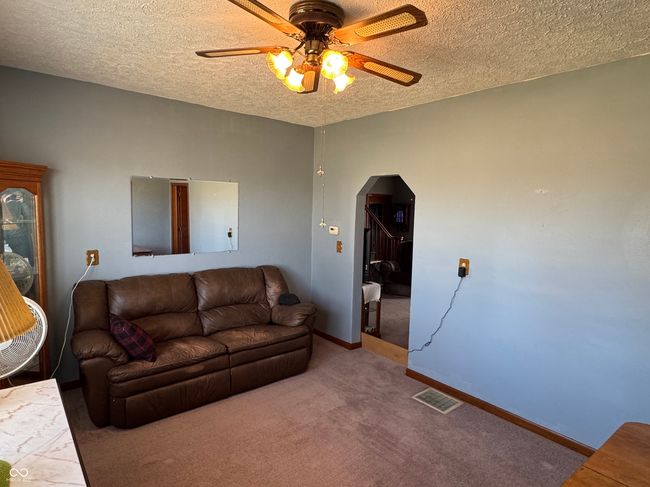 carpeted living room featuring a textured ceiling, baseboards, visible vents, arched walkways, and ceiling fan | Image 21
