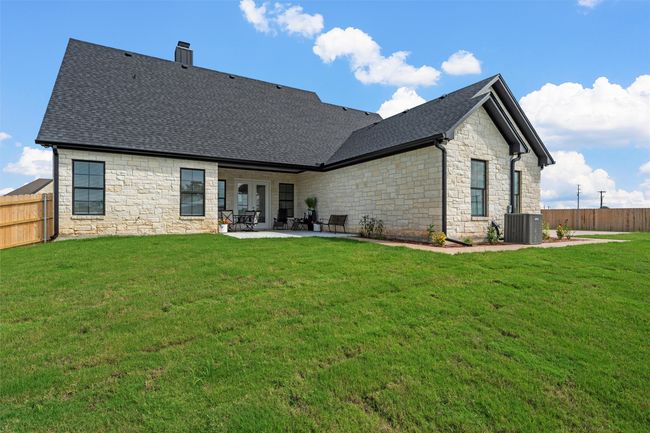 Back of property featuring stone siding, a patio area, a fenced backyard, roof with shingles, and a chimney | Image 36