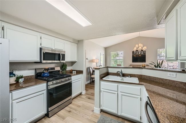 Kitchen with a sink, light wood-style floors, an inviting chandelier, a peninsula, and appliances with stainless steel finishes | Image 8
