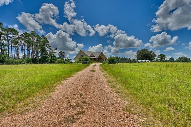 Welcome to your serene retreat, where a charming country home awaits at the end of a picturesque gravel driveway, surrounded by lush greenery and open skies. | Image 30