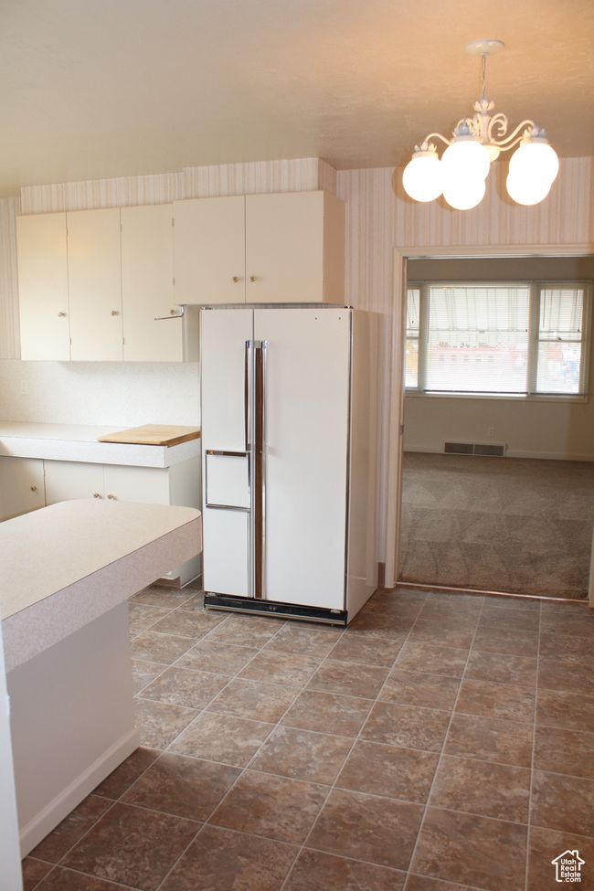 Kitchen with freestanding refrigerator, a chandelier, light countertops, pendant lighting, and cream cabinets | Image 6