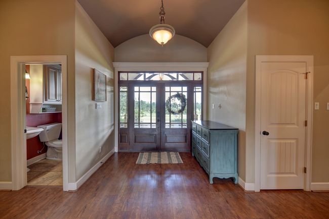 A welcoming entryway featuring a large glass-paneled front door and a high ceiling with a hanging light fixture. | Image 14