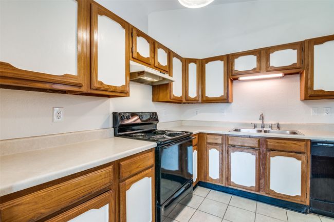 Kitchen with black appliances, under cabinet range hood, light tile patterned flooring, and light countertops | Image 13