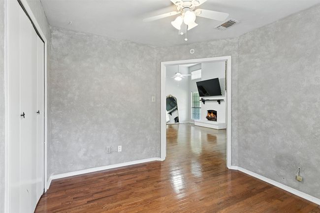 Unfurnished room with a ceiling fan, wood finished floors, and a warm lit fireplace | Image 7