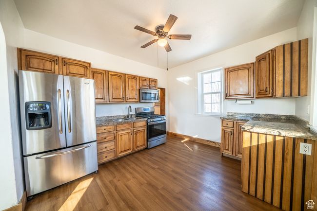Kitchen featuring dark wood finished floors, a ceiling fan, brown cabinets, stainless steel appliances, and a sink | Image 6