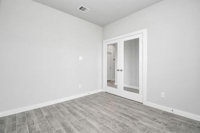 Experience the perfect blend of sophistication and warmth in this home office, boasting elegant wood-look tile flooring and flooded with natural light from expansive windows and French doors. Sample photo of completed home with similar floor plan. Actual colors and selections may vary. | Image 3