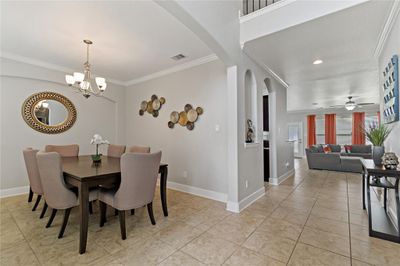 This is a spacious and well-lit open floor plan home featuring a tiled dining area with a modern chandelier and a large mirror on the wall, leading into a living space with contemporary furnishings and a view of the upper level. Bright accents and natural light create an inviting atmosphere. | Image 3