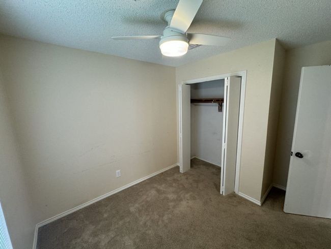 Unfurnished bedroom with dark colored carpet, a closet, ceiling fan, and a textured ceiling | Image 25