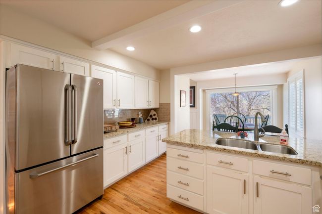 Kitchen with freestanding refrigerator, decorative backsplash, white cabinetry, a sink, and light wood finished floors | Image 19