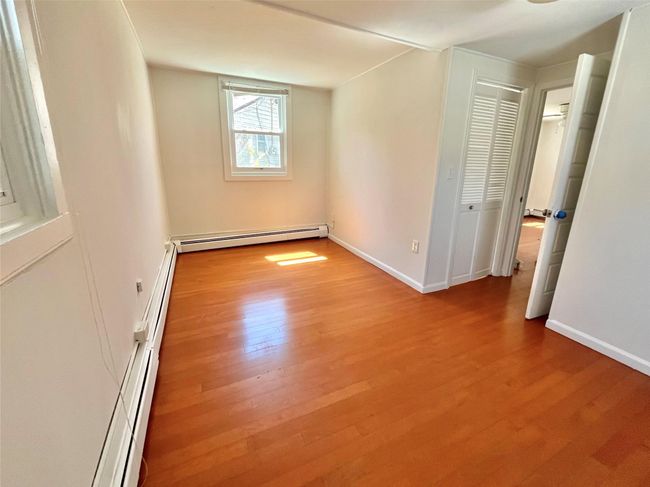 Unfurnished bedroom with baseboard heating, baseboards, and wood finished floors | Image 4