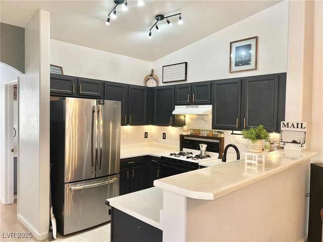 Kitchen with a peninsula, range with gas cooktop, under cabinet range hood, vaulted ceiling, and freestanding refrigerator | Image 6