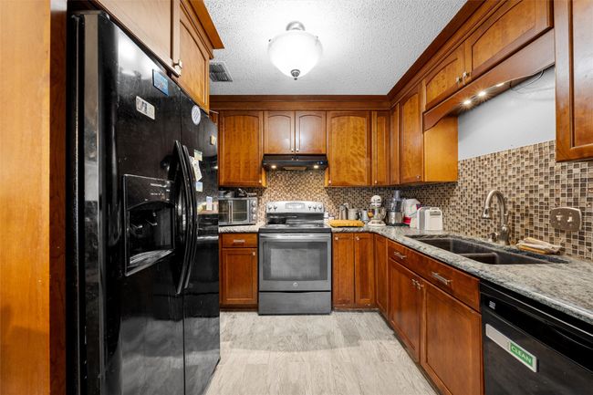 Kitchen with black appliances, a sink, under cabinet range hood, light wood finished floors, and tasteful backsplash | Image 7