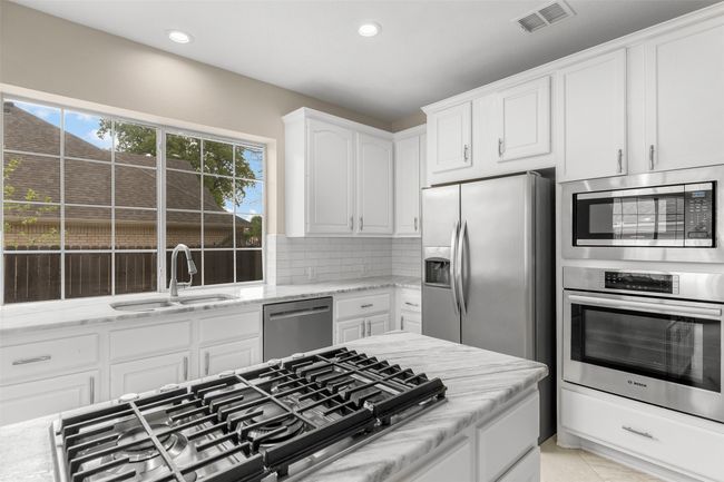 Kitchen with white cabinetry, stainless steel appliances, decorative backsplash, a sink, and visible vents | Image 13