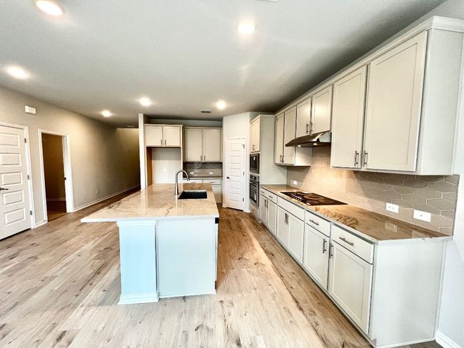 Kitchen featuring tasteful backsplash, light stone counters, an island with sink, recessed lighting, and light wood-type flooring | Image 5