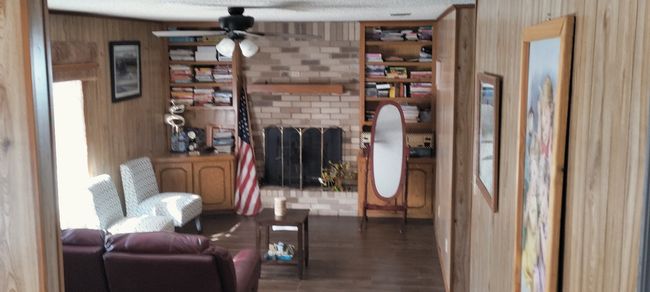 Living area with ceiling fan, a fireplace, wooden walls, and wood finished floors | Image 15