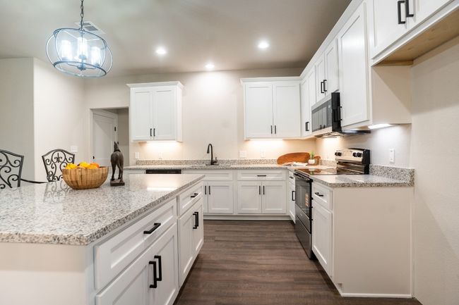 Kitchen with stainless steel appliances, a sink, white cabinetry, dark wood-style floors, and hanging light fixtures | Image 7