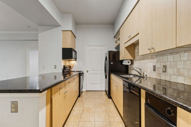 Kitchen with black appliances, a peninsula, light brown cabinets, decorative backsplash, and dark stone counters | Image 12