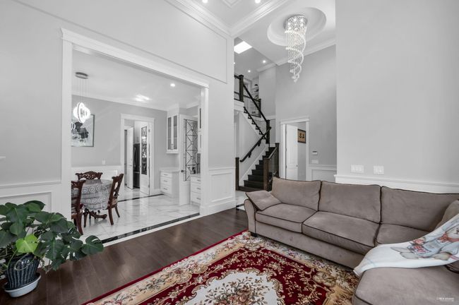 Living room with crown molding, a chandelier, a decorative wall, wainscoting, and stairs | Image 6