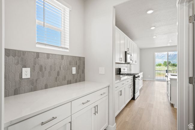 Kitchen with gas range oven, stainless steel microwave, recessed lighting, light wood-style floors, and white cabinetry | Image 9