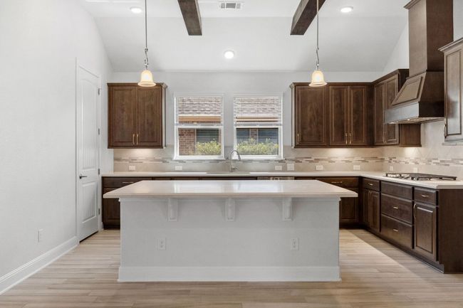 Kitchen with custom exhaust hood, light countertops, vaulted ceiling with beams, and stainless steel gas cooktop | Image 15