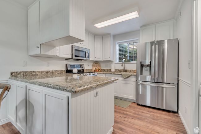 Kitchen with stainless steel appliances, white cabinetry, and light wood finished floors | Image 5