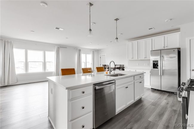 Kitchen with appliances with stainless steel finishes, a kitchen island with sink, wood finished floors, and white cabinetry | Image 15