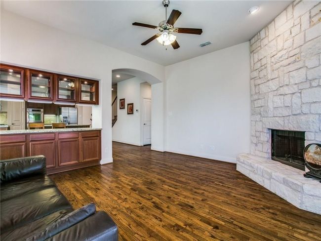Living room with arched walkways, ceiling fan, dark wood-type flooring, a stone fireplace, and baseboards | Image 11