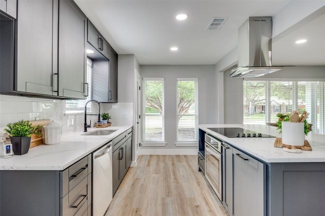 Kitchen with island exhaust hood, appliances with stainless steel finishes, gray cabinetry, light wood-style flooring, and decorative backsplash | Image 14