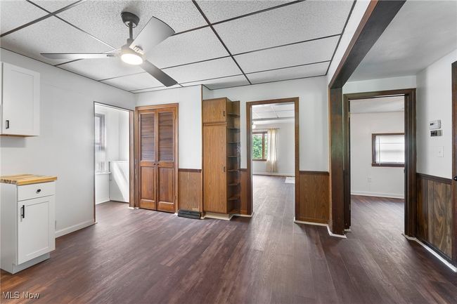 Kitchen with a ceiling fan, a wainscoted wall, dark wood-type flooring, white cabinetry, and a paneled ceiling | Image 10