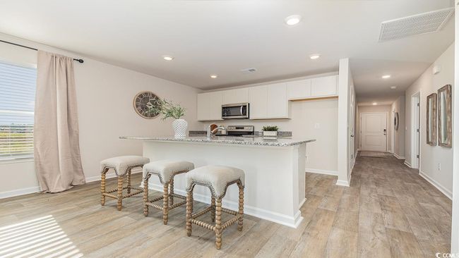 Kitchen featuring white cabinetry, stainless steel appliances, light stone counters, a center island with sink, and light wood-type flooring | Image 9