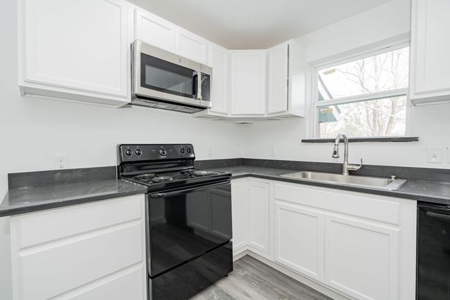 Kitchen featuring dark countertops, stainless steel microwave, electric range, white cabinets, and a sink | Image 8