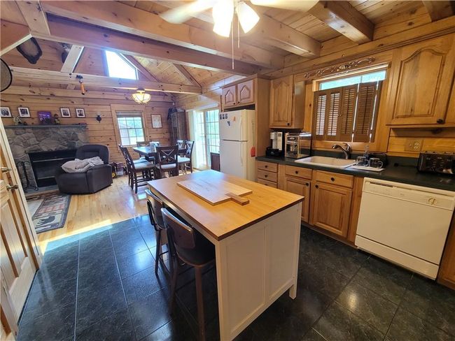 Kitchen featuring a stone fireplace, ceiling fan, white appliances, lofted ceiling with beams, and dark tile flooring | Image 11