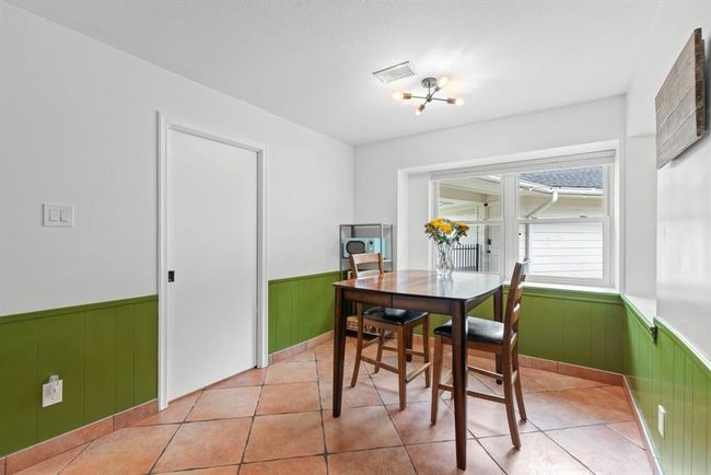 This cozy breakfast area features a modern light fixture, wrap around windows providing plenty of natural light.The space is accented with green wainscoting and terracotta tile flooring, creating a warm and inviting atmosphere. | Image 12