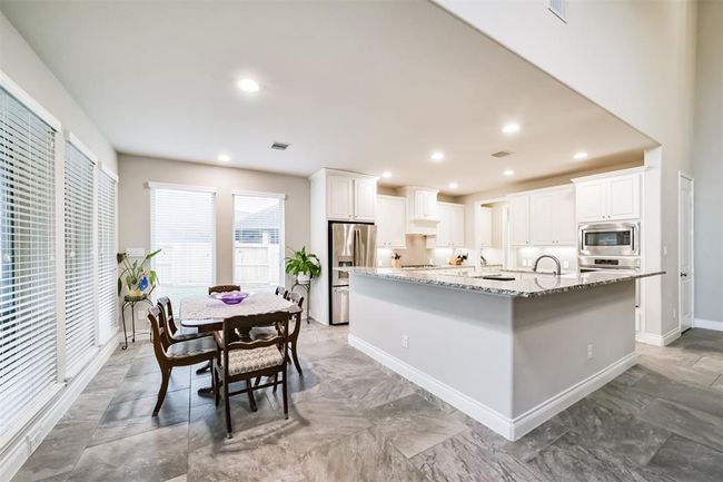 This photo showcases a spacious, open-concept kitchen with modern amenities. It features granite countertops, a large island, and stainless steel appliances. The room is bright with ample natural light from multiple windows, and it flows seamlessly into a dining area, making it perfect for entertaining. | Image 12