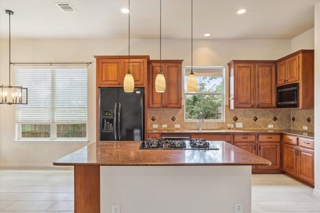 Kitchen with black fridge, gas stovetop, brown cabinets, a kitchen island, and backsplash | Image 13
