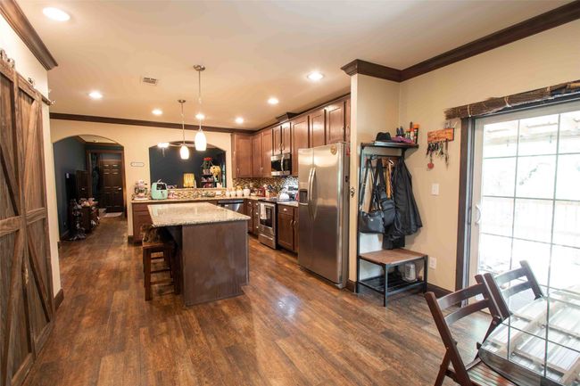 Kitchen featuring stainless steel appliances, arched walkways, ornamental molding, a kitchen breakfast bar, and dark wood-style floors | Image 11