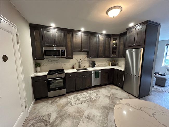 Kitchen with glass insert cabinets, dark brown cabinets, a sink, stainless steel appliances, and decorative backsplash | Image 7