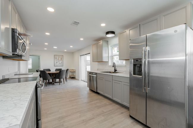Kitchen with stainless steel appliances, gray cabinetry, light wood-style flooring, recessed lighting, and light stone countertops | Image 16