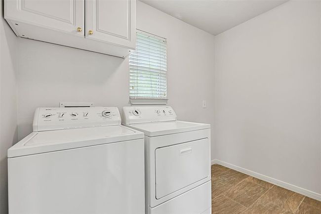 Spacious utility room located just off the kitchen, featuring upper cabinetry, natural light, and plenty of room for a second fridge or freezer — plus a tankless water heater for on-demand efficiency. | Image 15