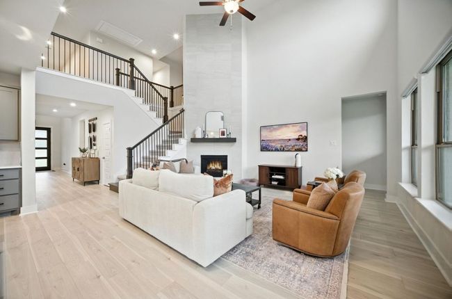 Living room featuring a high ceiling, light wood finished floors, ceiling fan, a fireplace, and stairs | Image 8