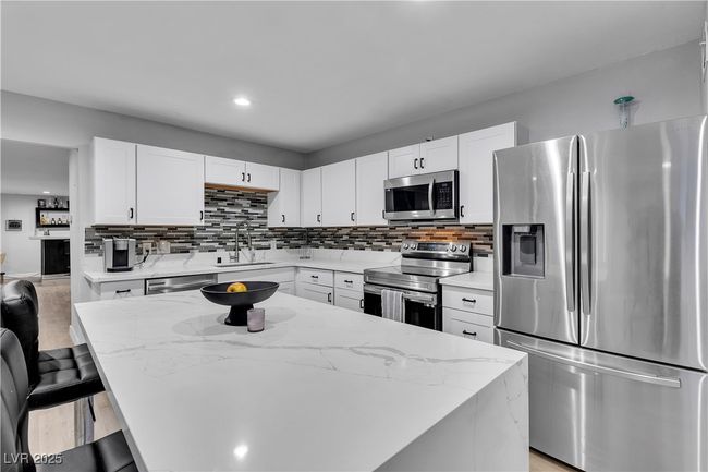 Kitchen with light stone counters, tasteful backsplash, white cabinets, a sink, and appliances with stainless steel finishes | Image 11