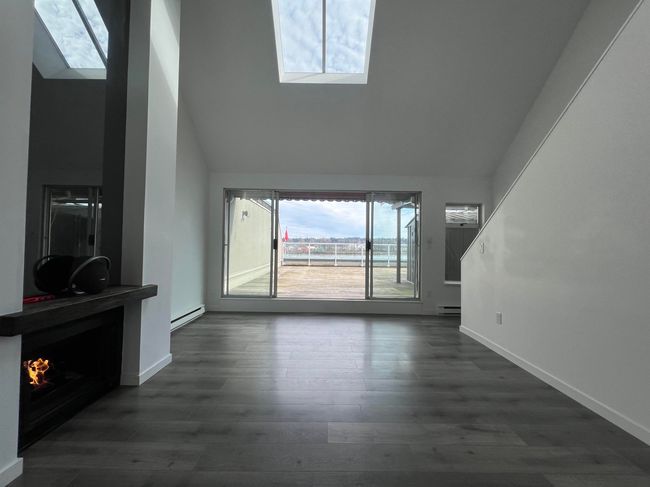 Unfurnished living room featuring a skylight, baseboard heating, dark wood-type flooring, and high vaulted ceiling | Image 17