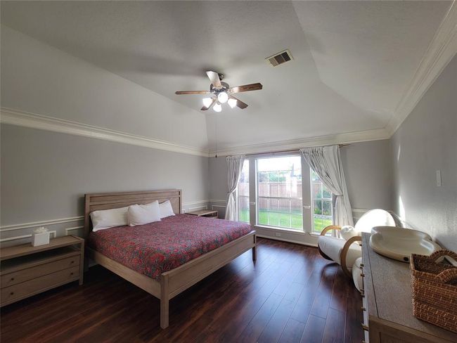 This photo shows a spacious bedroom with a vaulted ceiling and large window providing ample natural light. The room features wood flooring, a ceiling fan, and neutral-colored walls, creating a cozy and inviting atmosphere. | Image 17