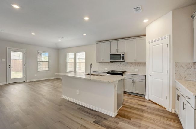 Kitchen featuring a kitchen island with sink, backsplash, light stone countertops, recessed lighting, and stainless steel microwave | Image 20